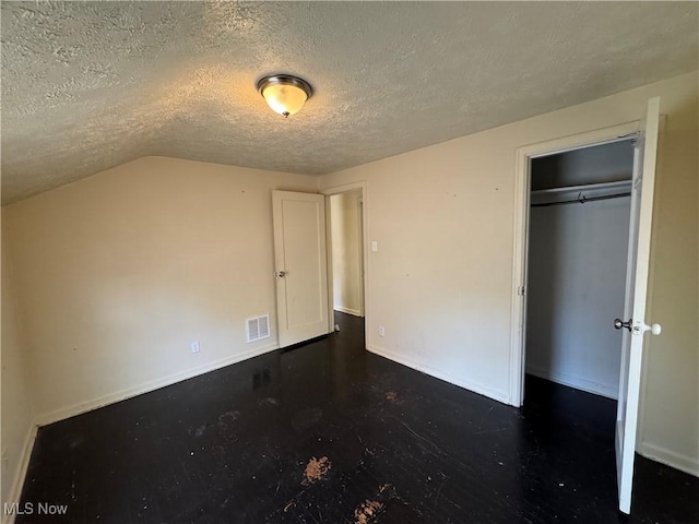 unfurnished bedroom with lofted ceiling, a closet, and a textured ceiling