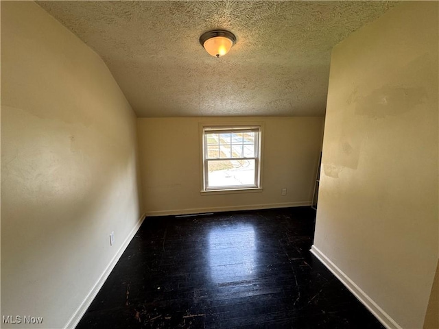 spare room with dark wood-type flooring, vaulted ceiling, and a textured ceiling