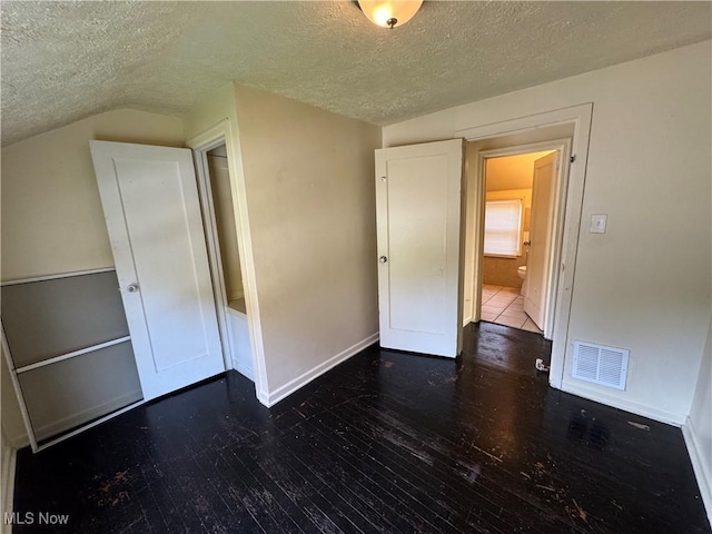 unfurnished room featuring dark hardwood / wood-style floors, vaulted ceiling, and a textured ceiling