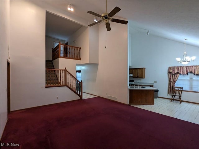 unfurnished living room with sink, ceiling fan with notable chandelier, light colored carpet, and high vaulted ceiling