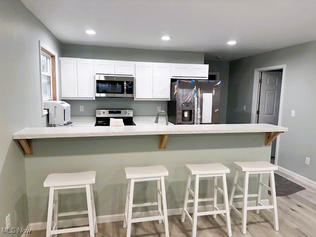 kitchen featuring sink, a breakfast bar area, stainless steel appliances, light hardwood / wood-style floors, and white cabinets