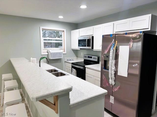 kitchen with a kitchen bar, sink, white cabinetry, a wall mounted AC, and appliances with stainless steel finishes