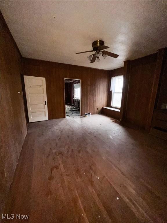 unfurnished room with dark hardwood / wood-style floors, ceiling fan, and wood walls