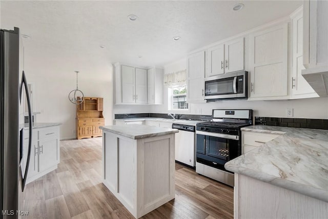 kitchen with light wood-type flooring, appliances with stainless steel finishes, a kitchen island, light stone countertops, and white cabinets