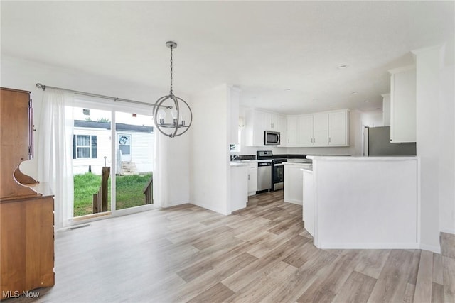 kitchen with appliances with stainless steel finishes, white cabinets, a chandelier, hanging light fixtures, and light wood-type flooring