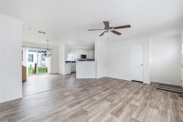 unfurnished living room with ceiling fan with notable chandelier and light wood-type flooring