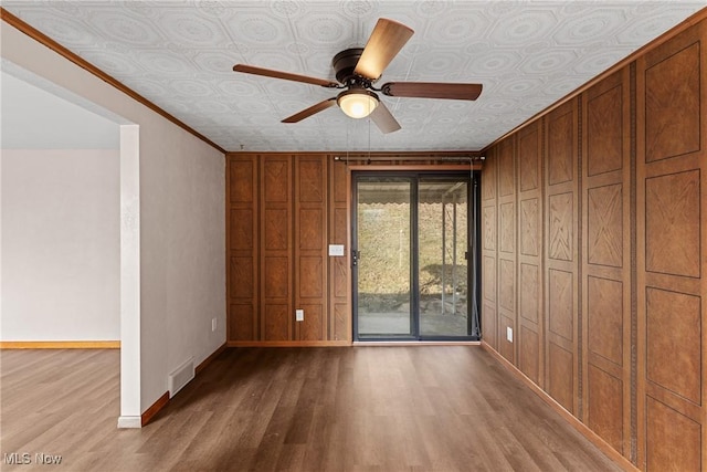 empty room featuring ornamental molding, wood walls, ceiling fan, and light hardwood / wood-style flooring