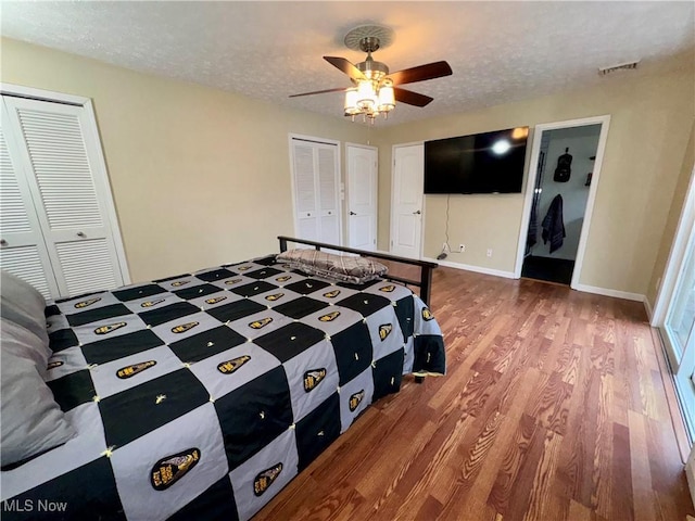 bedroom with hardwood / wood-style flooring, ceiling fan, a textured ceiling, and two closets