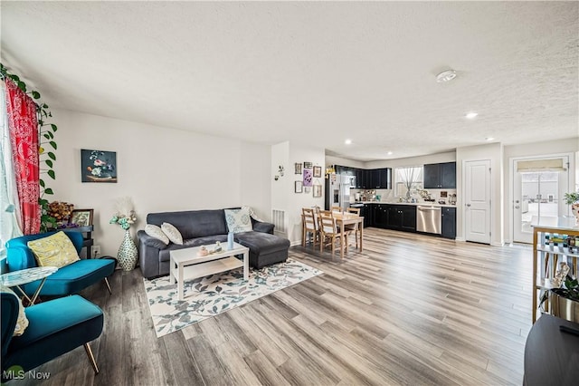 living room featuring sink, light hardwood / wood-style flooring, and a textured ceiling