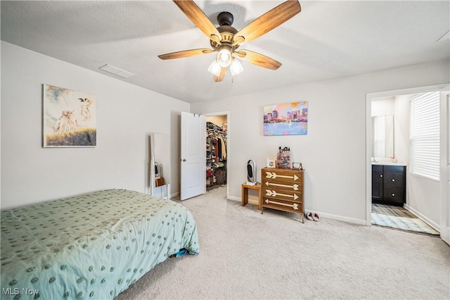 bedroom with a walk in closet, ensuite bath, light carpet, a closet, and ceiling fan