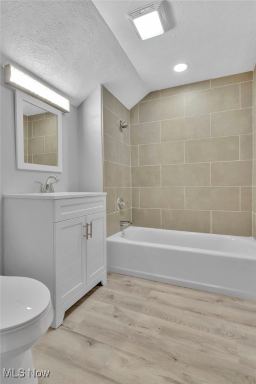 full bathroom featuring tiled shower / bath combo, vanity, hardwood / wood-style flooring, and a textured ceiling