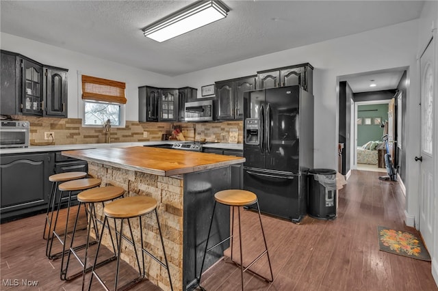 kitchen with a kitchen bar, dark hardwood / wood-style floors, black fridge with ice dispenser, and a kitchen island