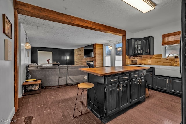 kitchen featuring a kitchen island, dark hardwood / wood-style floors, butcher block counters, a kitchen breakfast bar, and a brick fireplace