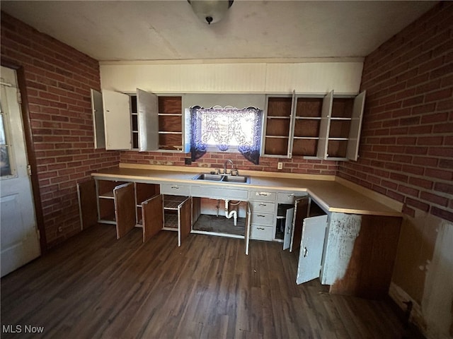 kitchen with sink, dark hardwood / wood-style floors, white cabinets, and brick wall