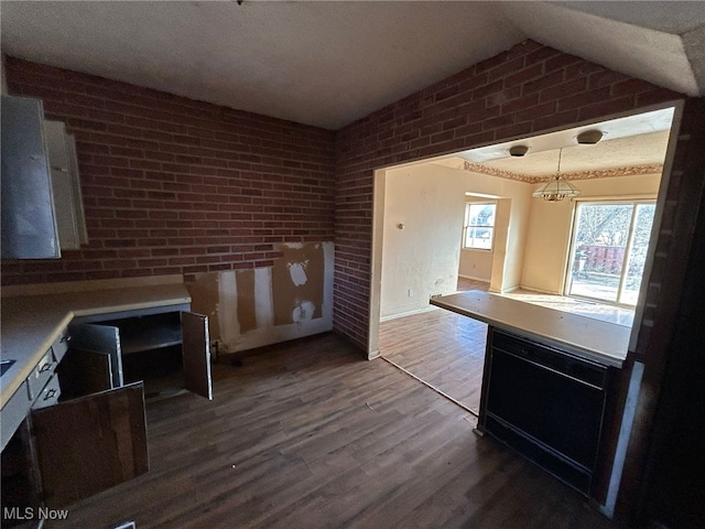 kitchen featuring pendant lighting, brick wall, vaulted ceiling, and hardwood / wood-style floors