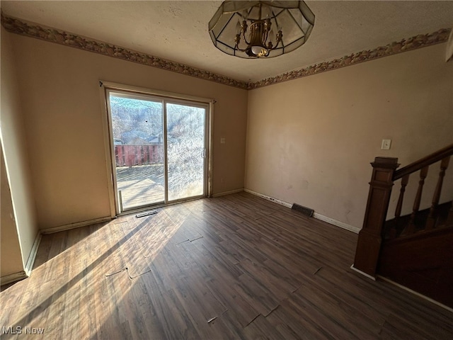 empty room with a notable chandelier and dark wood-type flooring