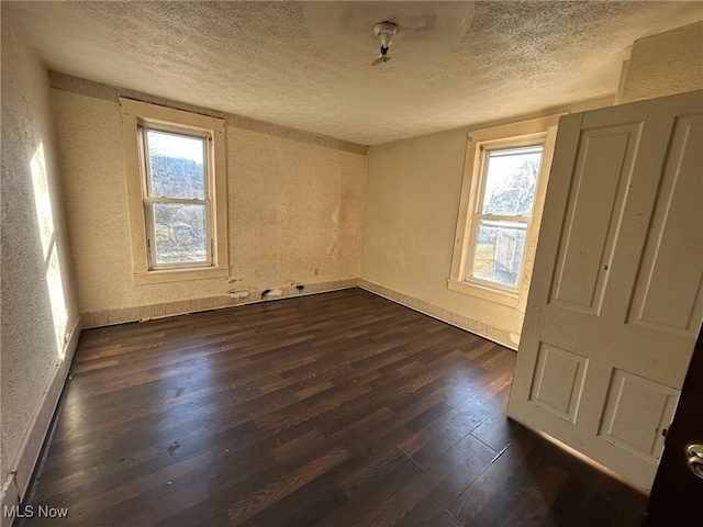 empty room with dark wood-type flooring, a healthy amount of sunlight, and a textured ceiling