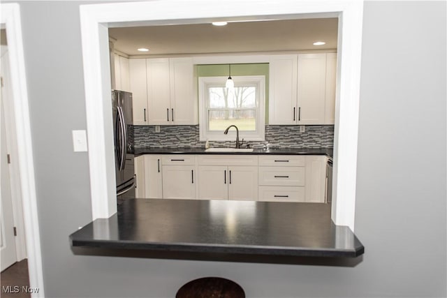 kitchen featuring black fridge, white cabinetry, sink, and decorative backsplash