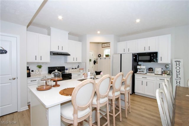 kitchen featuring an island with sink, sink, a breakfast bar area, white cabinets, and black appliances