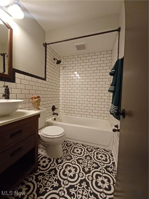 full bathroom with tile walls, tile patterned flooring, vanity, tiled shower / bath combo, and toilet