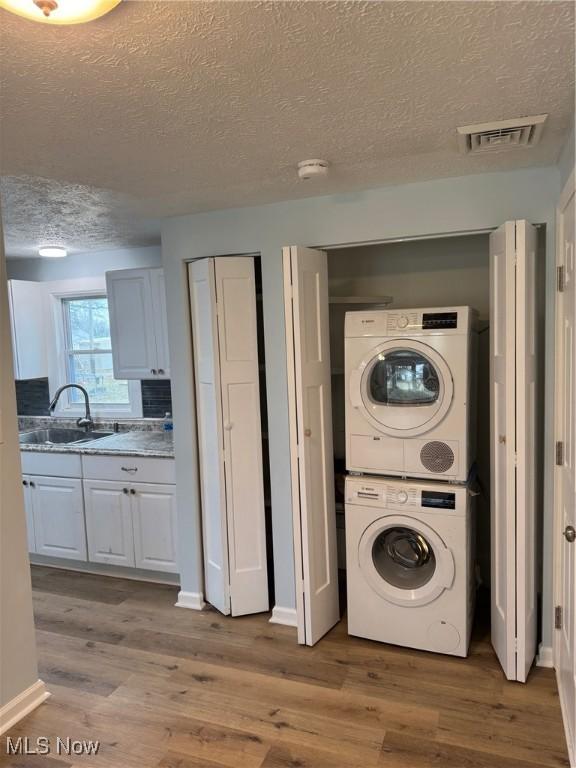 clothes washing area featuring sink, light hardwood / wood-style flooring, a textured ceiling, and stacked washer / dryer