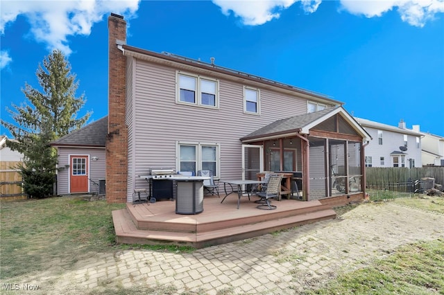 back of property with a wooden deck, a lawn, and a sunroom