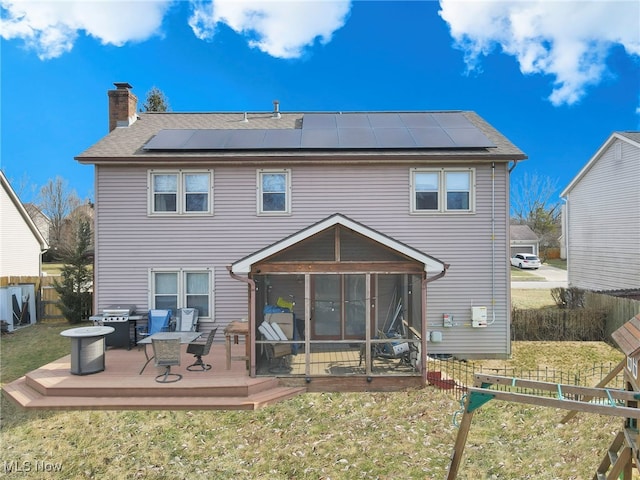 back of property with a wooden deck, a lawn, a sunroom, and solar panels