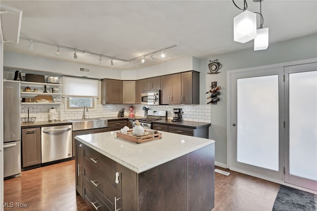 kitchen featuring sink, hanging light fixtures, stainless steel appliances, a center island, and decorative backsplash