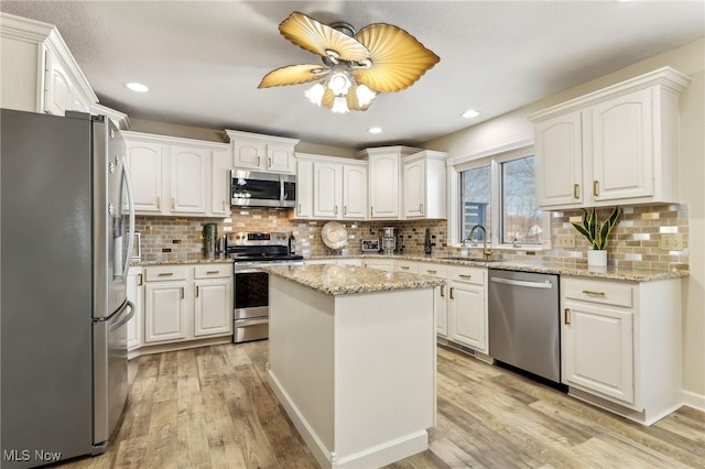 kitchen featuring appliances with stainless steel finishes, white cabinetry, sink, a center island, and light stone counters