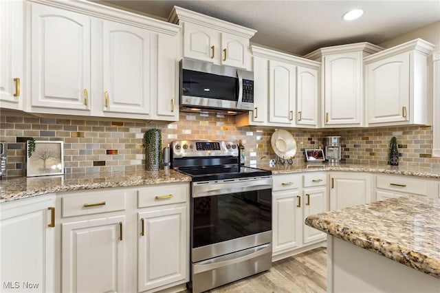 kitchen with white cabinetry, light stone counters, light hardwood / wood-style floors, and appliances with stainless steel finishes