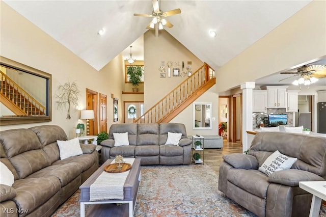 living room featuring high vaulted ceiling, ceiling fan with notable chandelier, light hardwood / wood-style flooring, and ornate columns