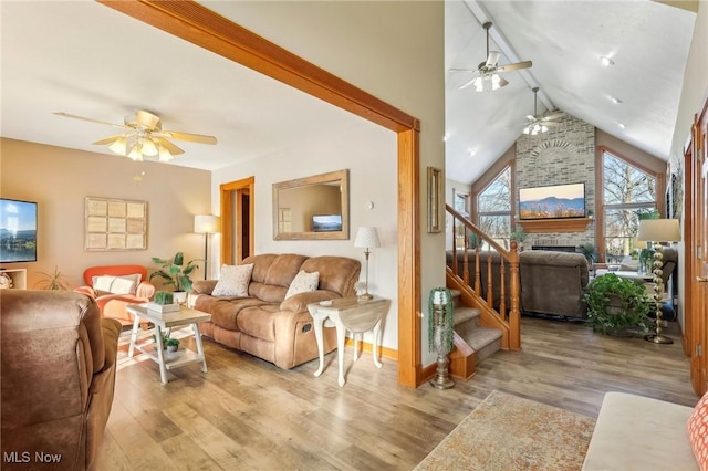 living room featuring high vaulted ceiling, a fireplace, light hardwood / wood-style floors, and ceiling fan