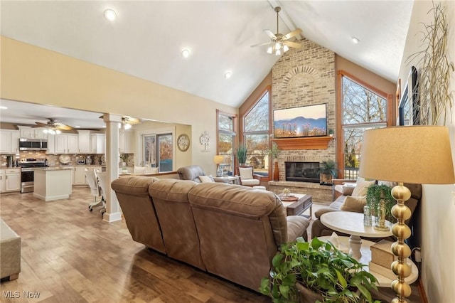 living room with high vaulted ceiling, a fireplace, light wood-type flooring, and a wealth of natural light