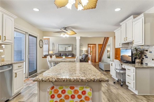 kitchen with built in desk, dishwasher, white cabinets, ceiling fan, and light stone counters