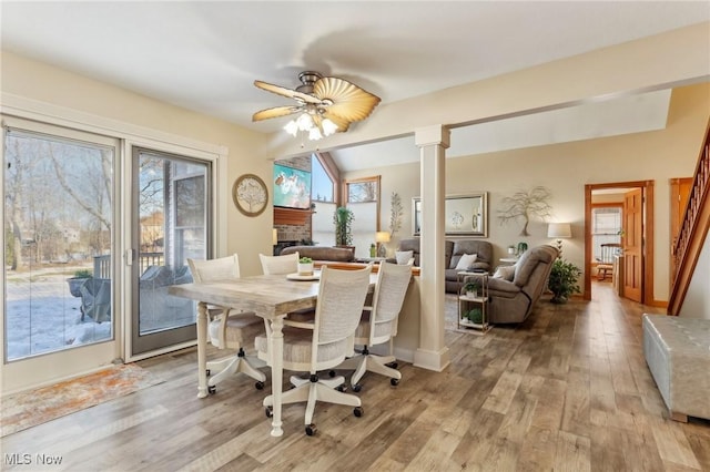 dining room with ornate columns, vaulted ceiling, a fireplace, ceiling fan, and light hardwood / wood-style floors