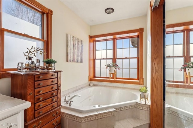 bathroom featuring a relaxing tiled tub, vanity, and a healthy amount of sunlight