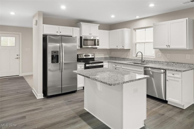 kitchen featuring a kitchen island, sink, white cabinets, light stone counters, and stainless steel appliances