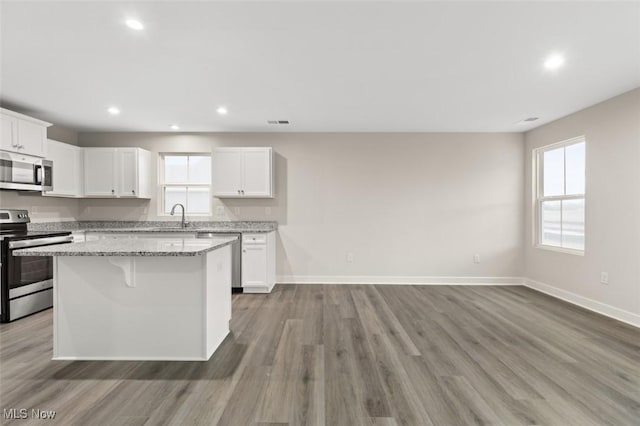 kitchen with white cabinetry, appliances with stainless steel finishes, a center island, and light stone countertops