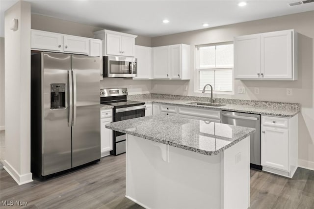 kitchen with sink, white cabinetry, stainless steel appliances, light stone counters, and a kitchen island