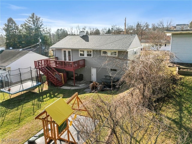 rear view of house featuring a wooden deck, a trampoline, and a lawn