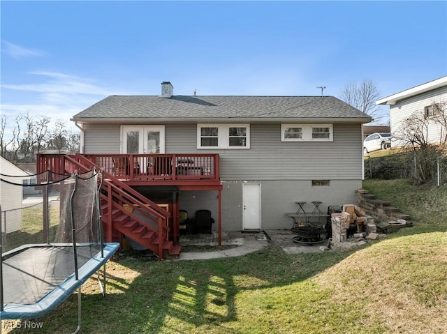 rear view of property with a deck, a yard, a trampoline, and a fire pit