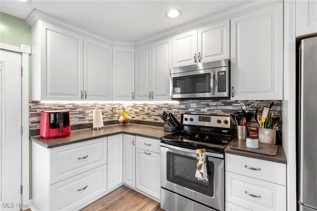 kitchen with stainless steel appliances, white cabinetry, backsplash, and light hardwood / wood-style floors