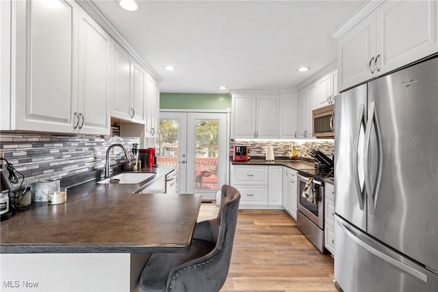 kitchen with sink, a breakfast bar area, white cabinetry, appliances with stainless steel finishes, and light hardwood / wood-style floors