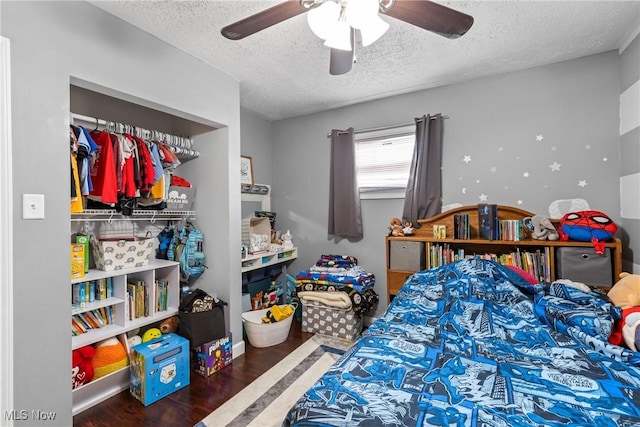 bedroom with dark wood-type flooring, ceiling fan, a closet, and a textured ceiling