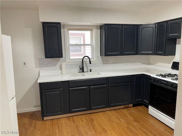 kitchen with range with gas stovetop, sink, backsplash, white fridge, and light hardwood / wood-style floors