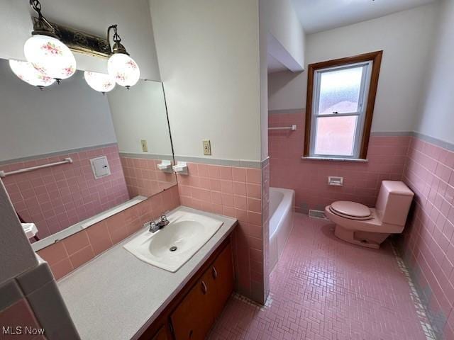 bathroom with tile patterned floors, toilet, tile walls, vanity, and a bathing tub