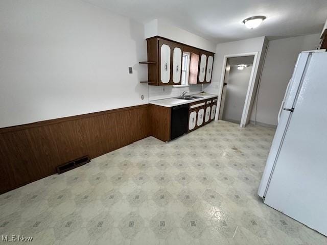 kitchen with dark brown cabinetry, wooden walls, sink, and white fridge