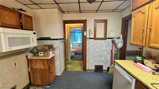 kitchen with a paneled ceiling, stainless steel dishwasher, carpet, and tile walls