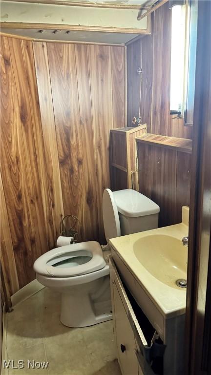 bathroom with tile patterned floors, vanity, toilet, and wood walls