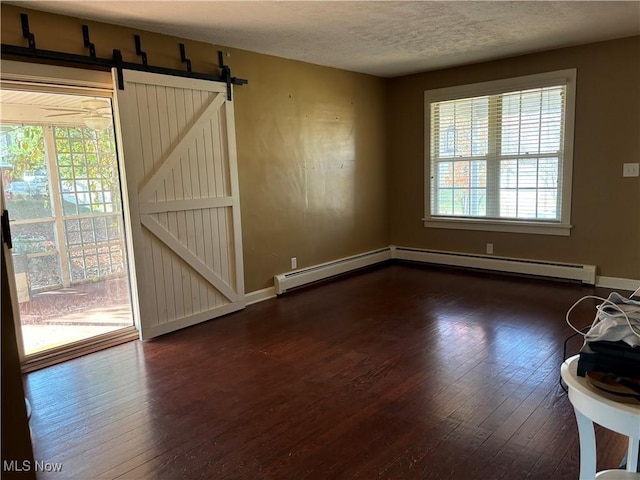 unfurnished room with a barn door, dark hardwood / wood-style floors, a wealth of natural light, and a textured ceiling